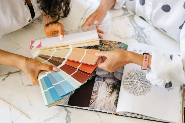 Two people selecting color swatches from a palette on a marble table, with a design book open, showcasing creative planning and interior design ideas.