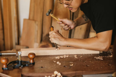 Craftsman using chisel and hammer to carve wooden board on traditional workbench