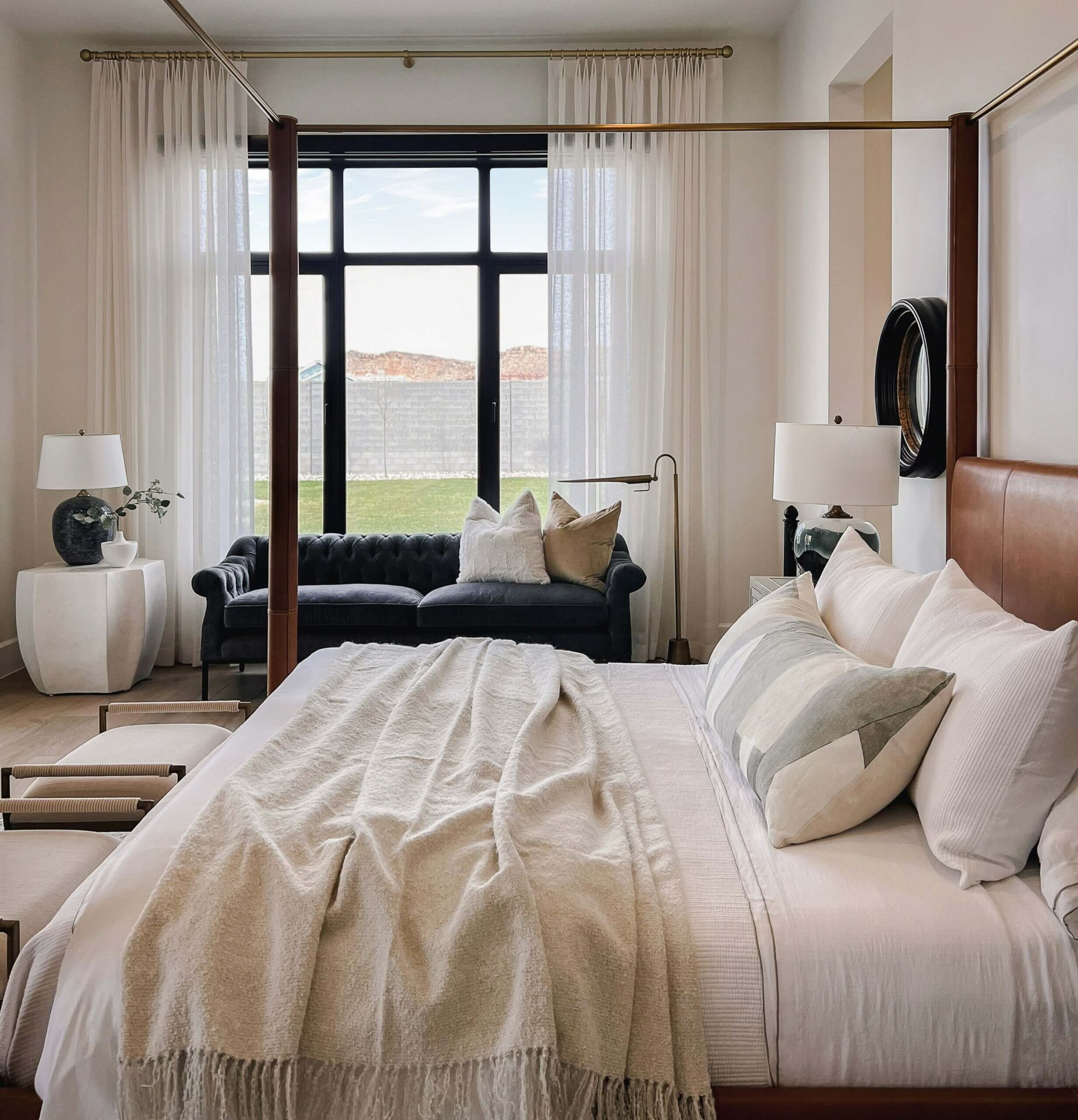 Elegant bedroom with a four-poster bed, cozy linens, and a sofa by large windows overlooking nature.